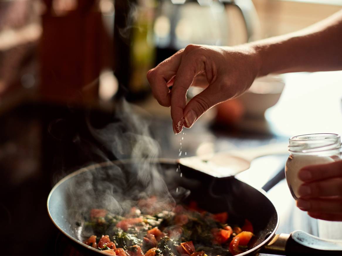 Ruka posipa začine po jelu koje se kuha u tavi.