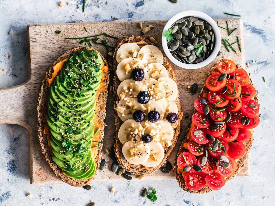 Tri tosta s avokadom, bananama i rajčicama na drvenoj dasci.