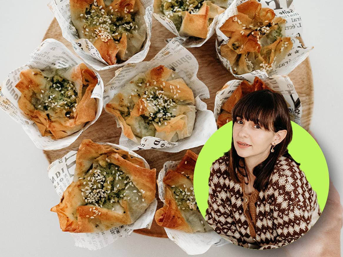 Žena s tamnom kosom i šiškama, u smeđem kardiganu, okružena je malim pecivima sa sezamom.