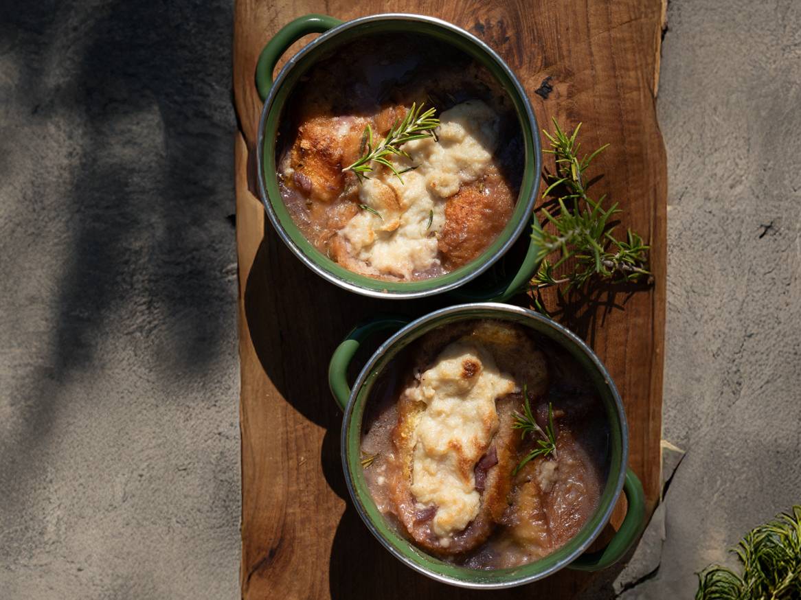 Dvije zdjelice francuske juhe od luka s kruhom i sirom, ukrašene ružmarinom.