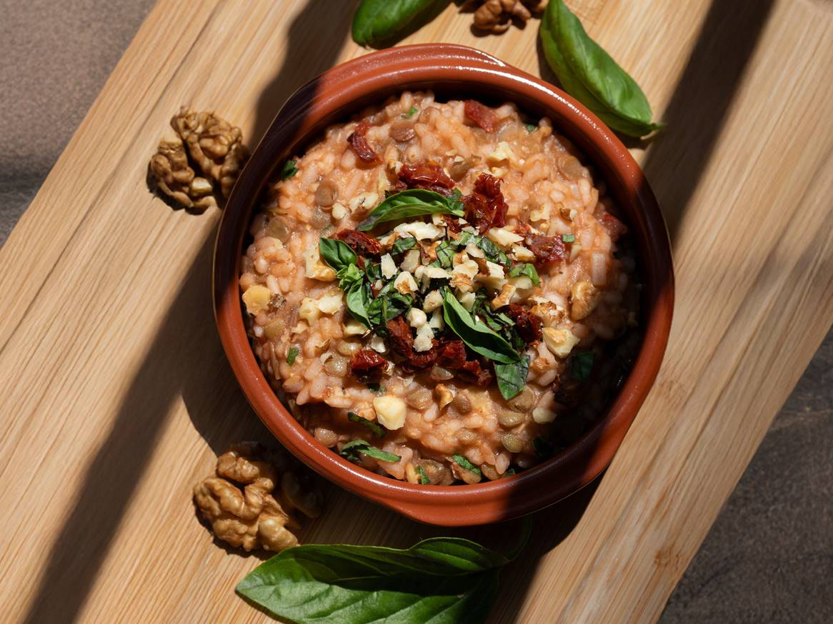 Rižoto od leće s orasima, sušenim rajčicama i bosiljkom u zdjeli na drvenoj dasci.