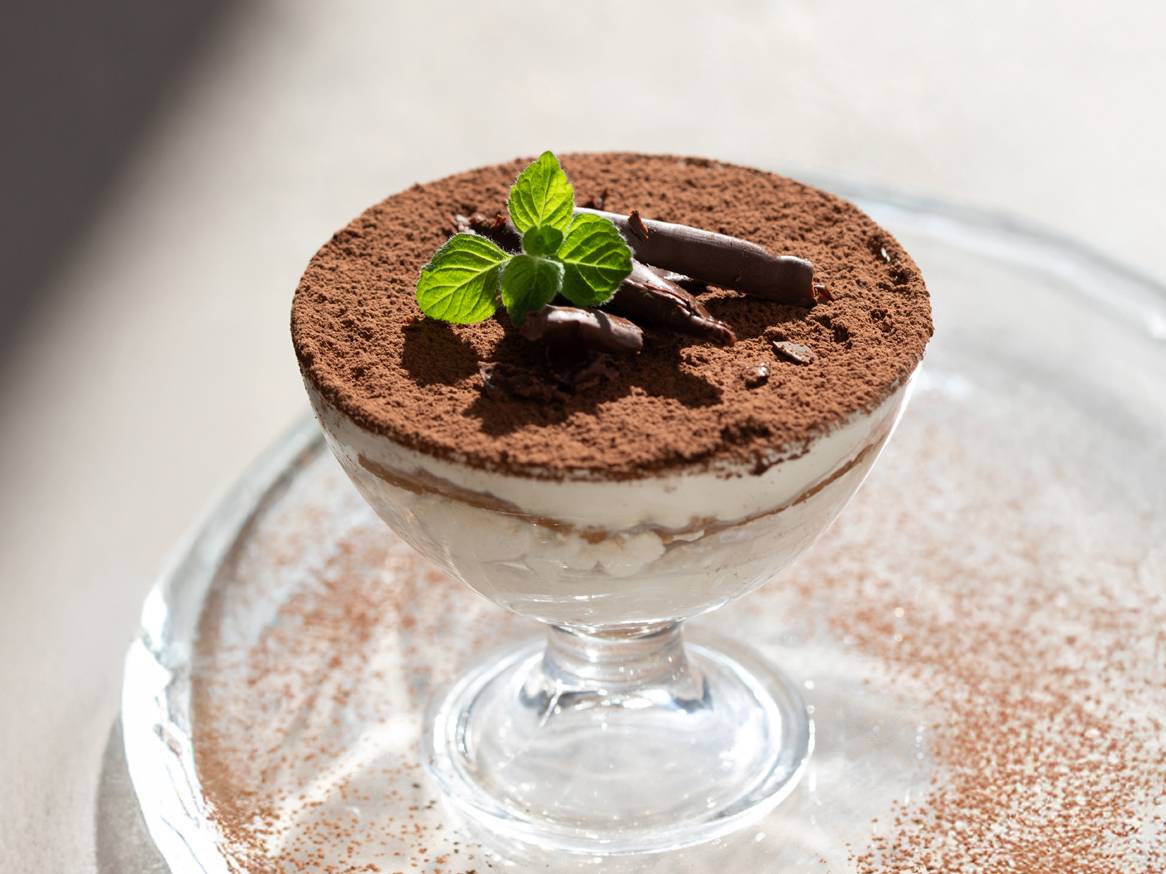 Tiramisu u staklenoj posudi s kakaom u prahu, čokoladnim strugotinama i listićima mente.