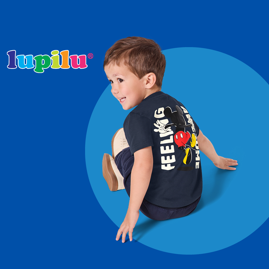 Dječak u tamnoplavoj majici s otiskom Mickeyja Mousea na leđima, sjedi na plavoj pozadini.