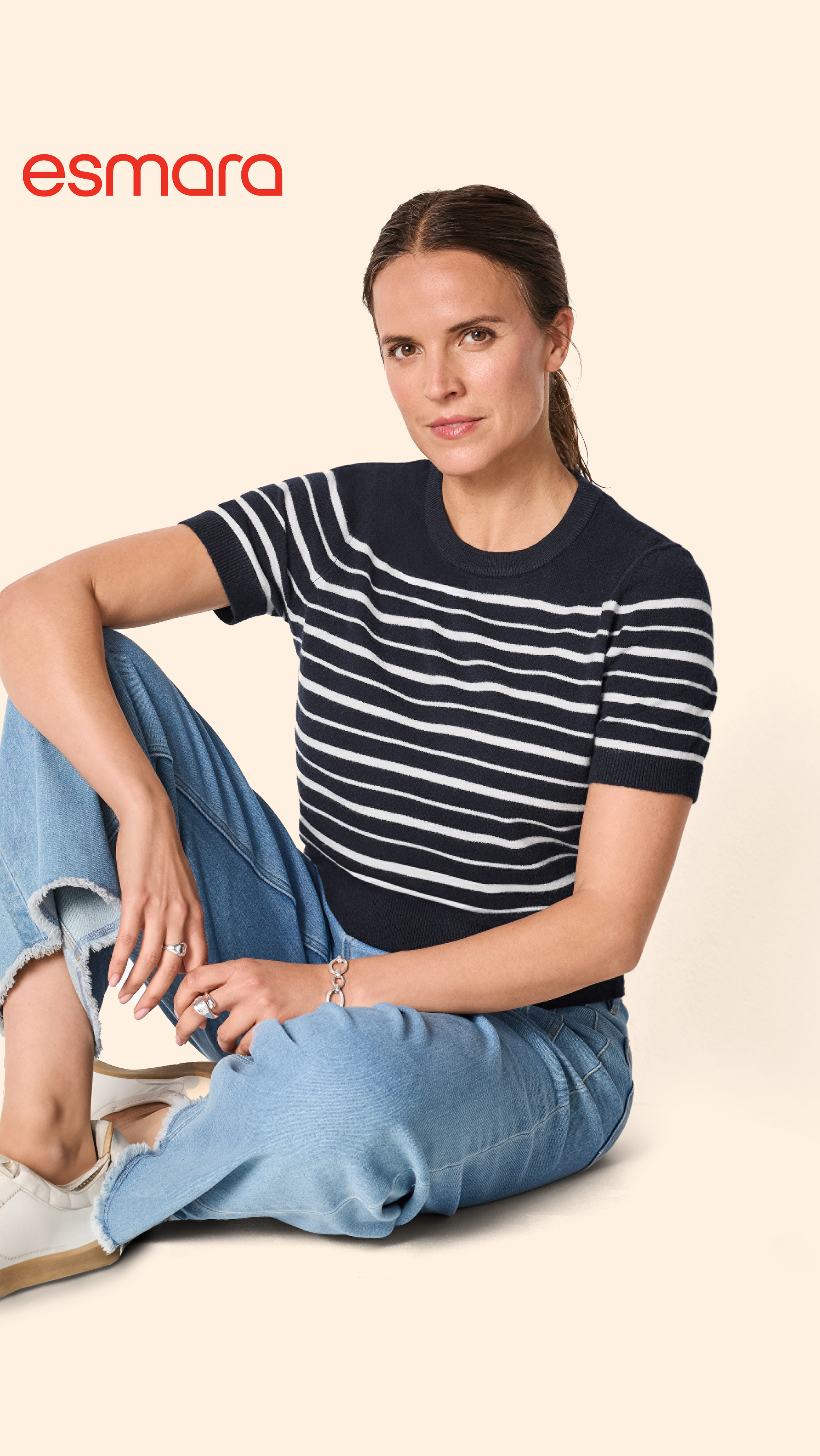 Žena u prugastoj majici kratkih rukava i trapericama sjedi na podu.