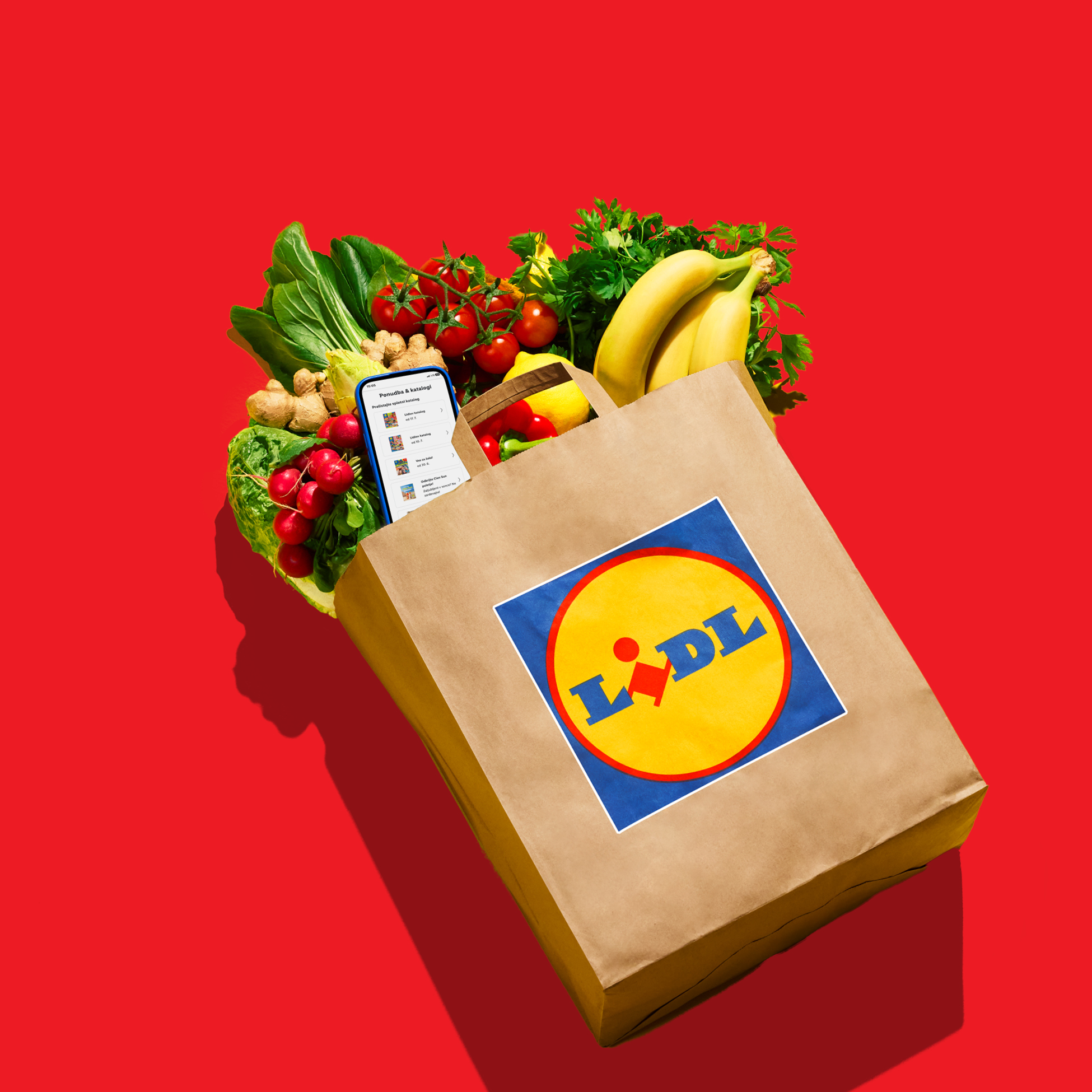 Papirnata vrećica puna svježeg voća i povrća, s mobitelom koji prikazuje katalog.