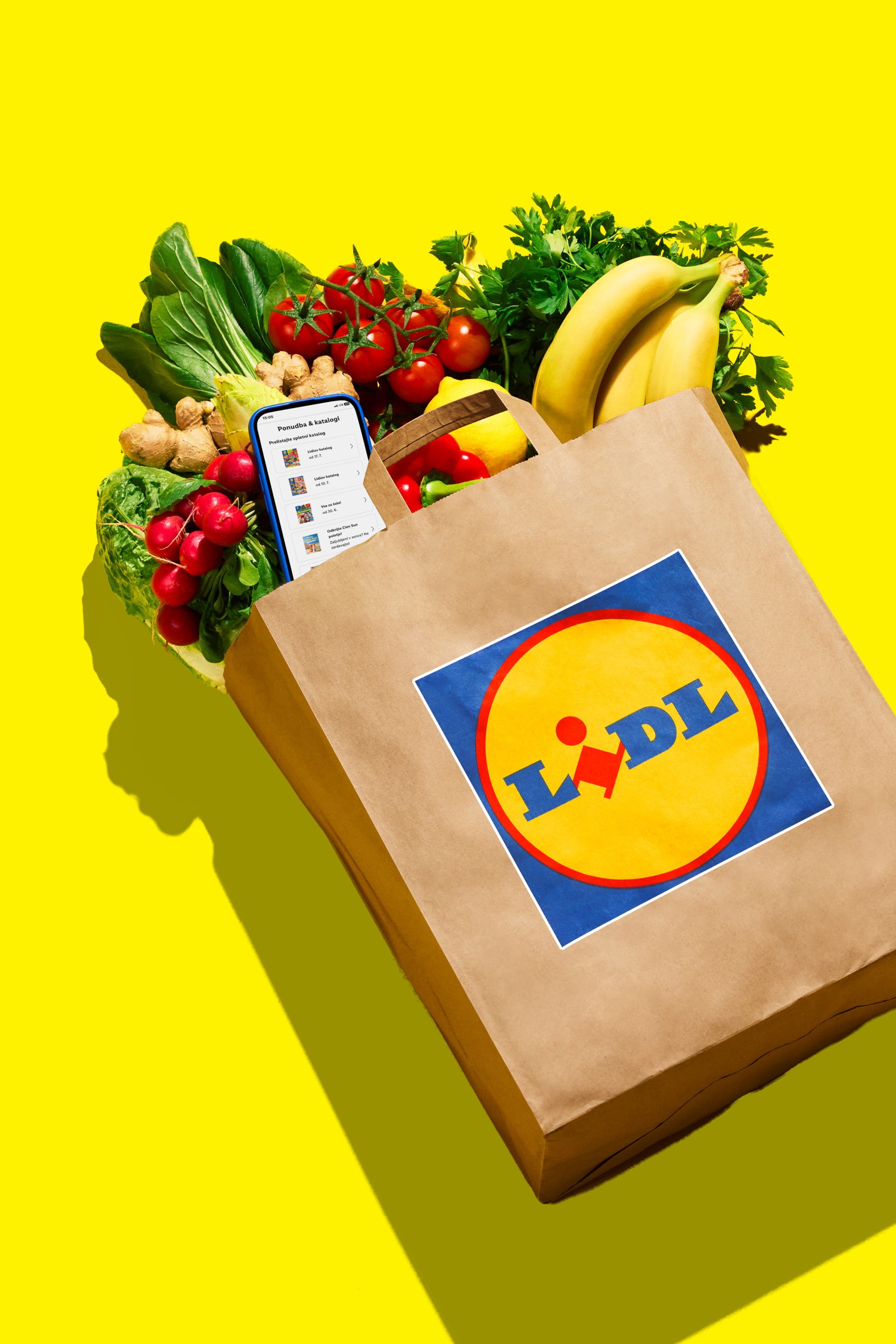 Papirnata vrećica s logotipom, puna svježeg voća i povrća, uz pametni telefon s aplikacijom za katalog.