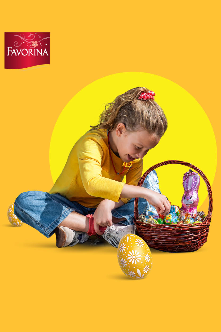 Djevojčica u žutoj majici i trapericama sjedi na podu i poseže za uskrsnom košarom punom čokoladnih zečeva i jaja.