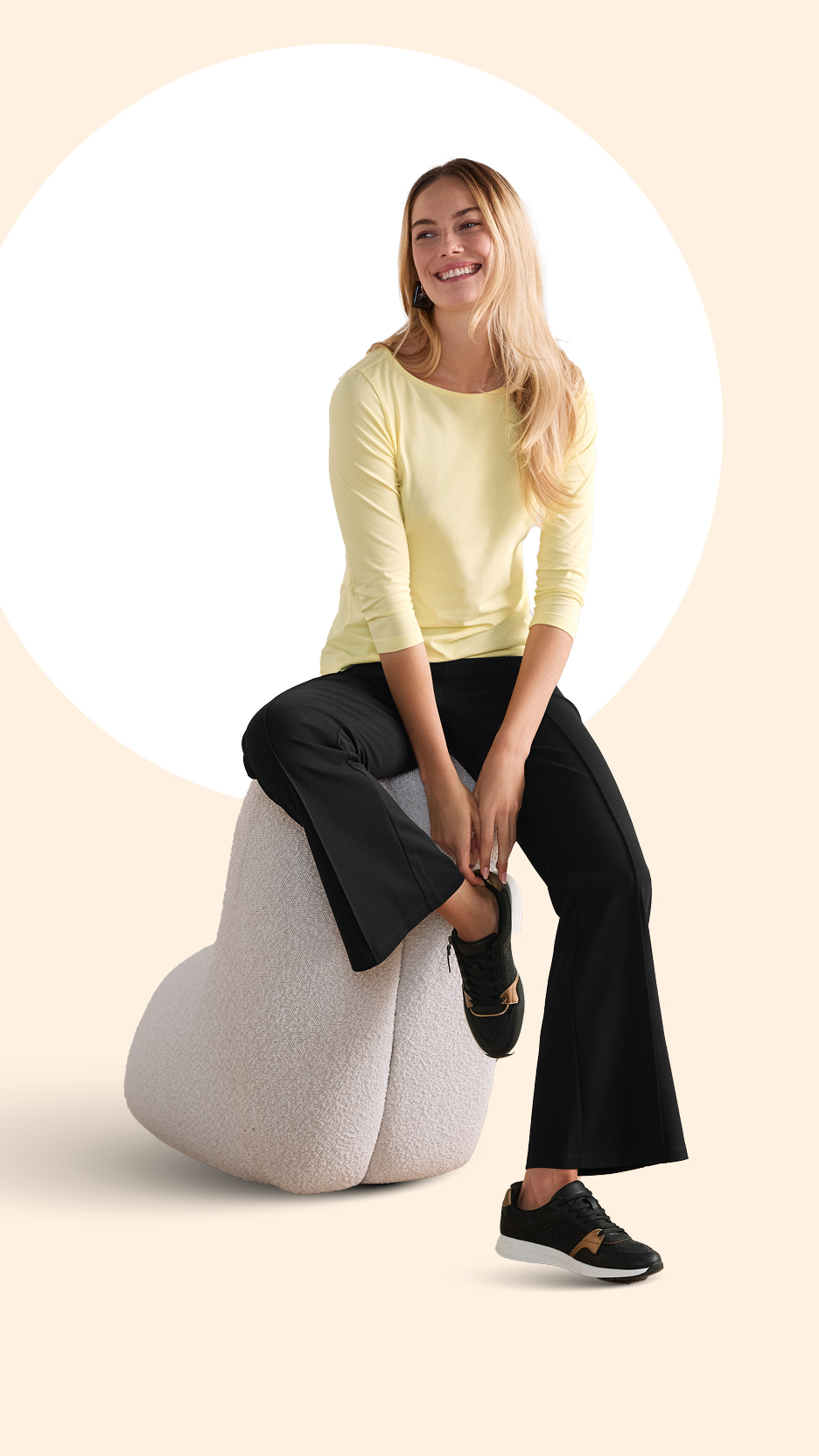 Žena u žutoj majici dugih rukava i crnim hlačama sjedi na bijeloj stolici, smiješeći se.